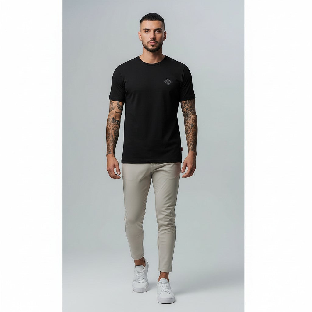Vallmountbotique black cotton t-shirt with embroidered geometric logo on chest. Model wearing relaxed fit tee and beige chinos.