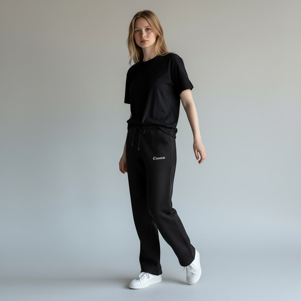 Vallmountbotique black sweatpants with drawstring waist and embroidered logo on leg. Model wears a black t-shirt and white sneakers.