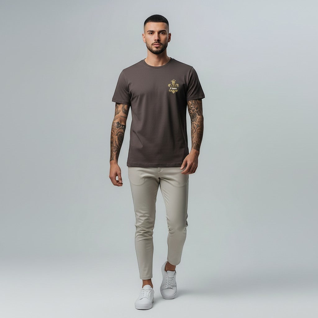 Vallmount boutique brown cotton t-shirt with gold embroidered fleur-de-lis on chest. Model wears t-shirt with beige trousers.
