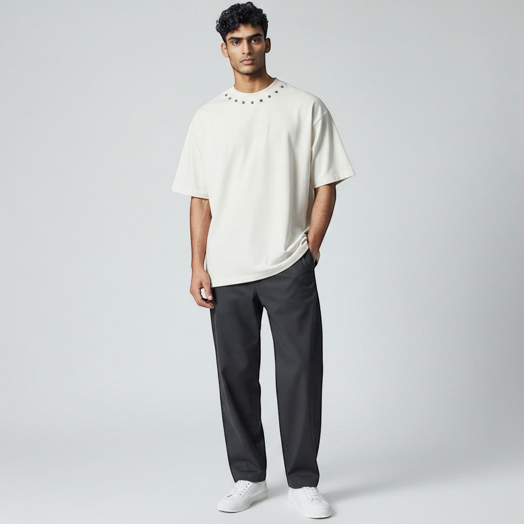 Vallmountbotique cream oversized cotton t-shirt with embellished neckline and embossed logo. Model wears dark trousers.