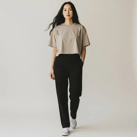 Vallmountbotique taupe cropped t-shirt with shoulder cutouts and embroidered logo, worn by a woman with black pants.
