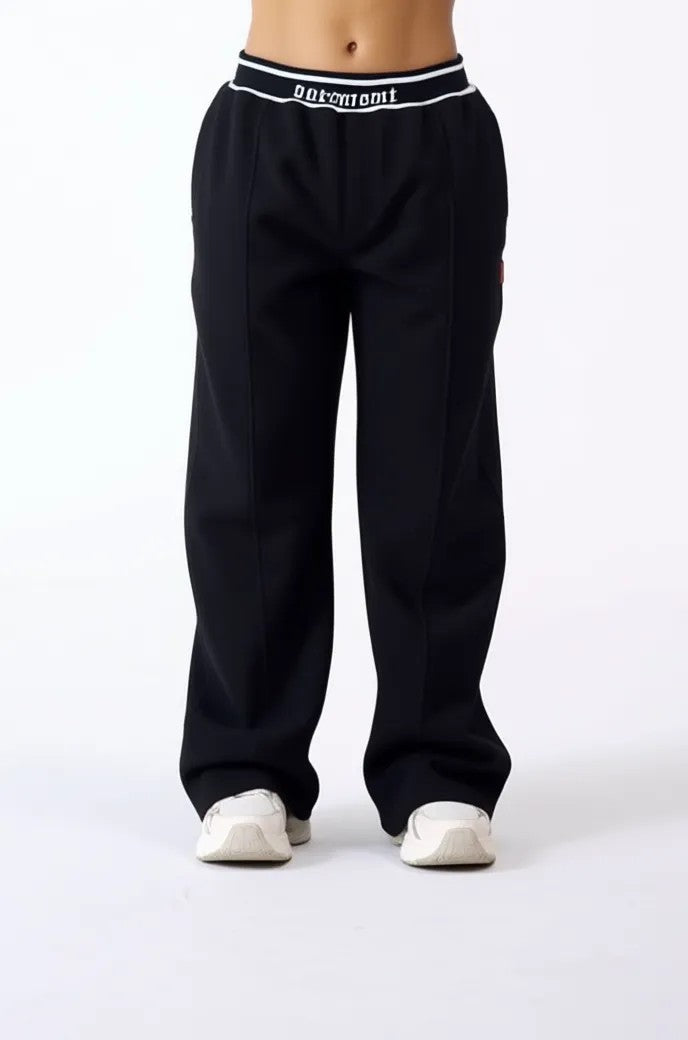 Vallmountboutique black wide-leg track pants with branded elastic waistband and white stripe detail.